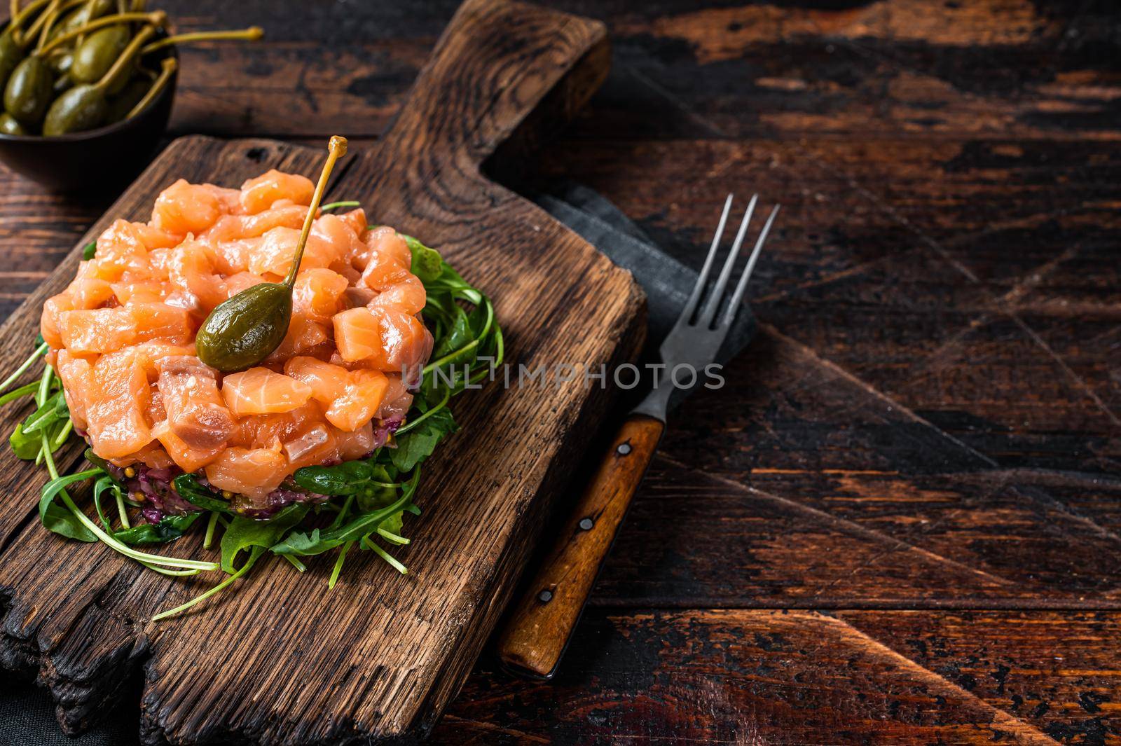 Salmon tartare or tartar with red onion, avocado, arugula and capers. Dark wooden background. Top View. Copy space.