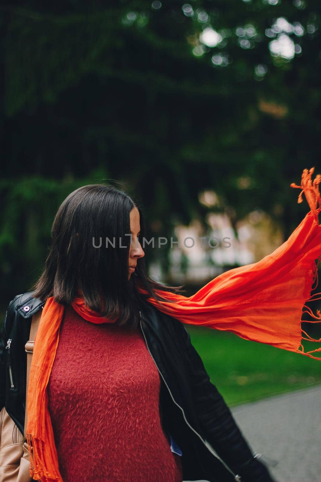 Portrait of a happy woman playing with bright orange scarf in the park