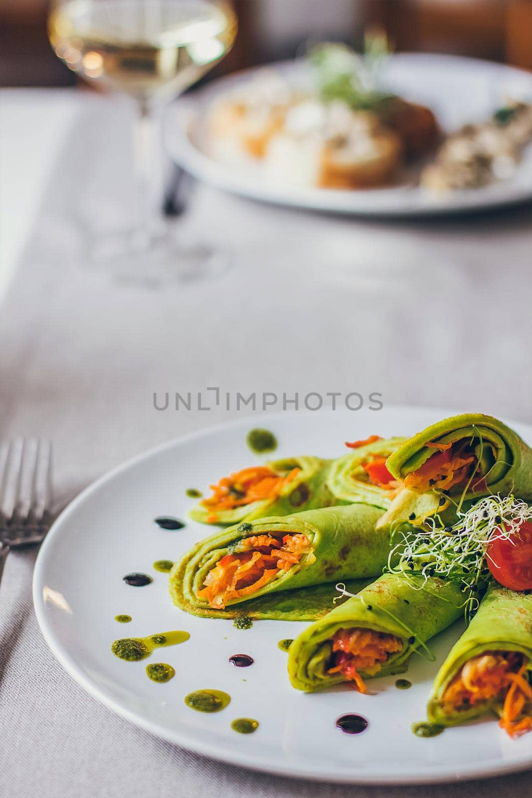 Healthy fresh green spinach pancakes stuffed with vegetables served on the table in the restaurant on the white plate