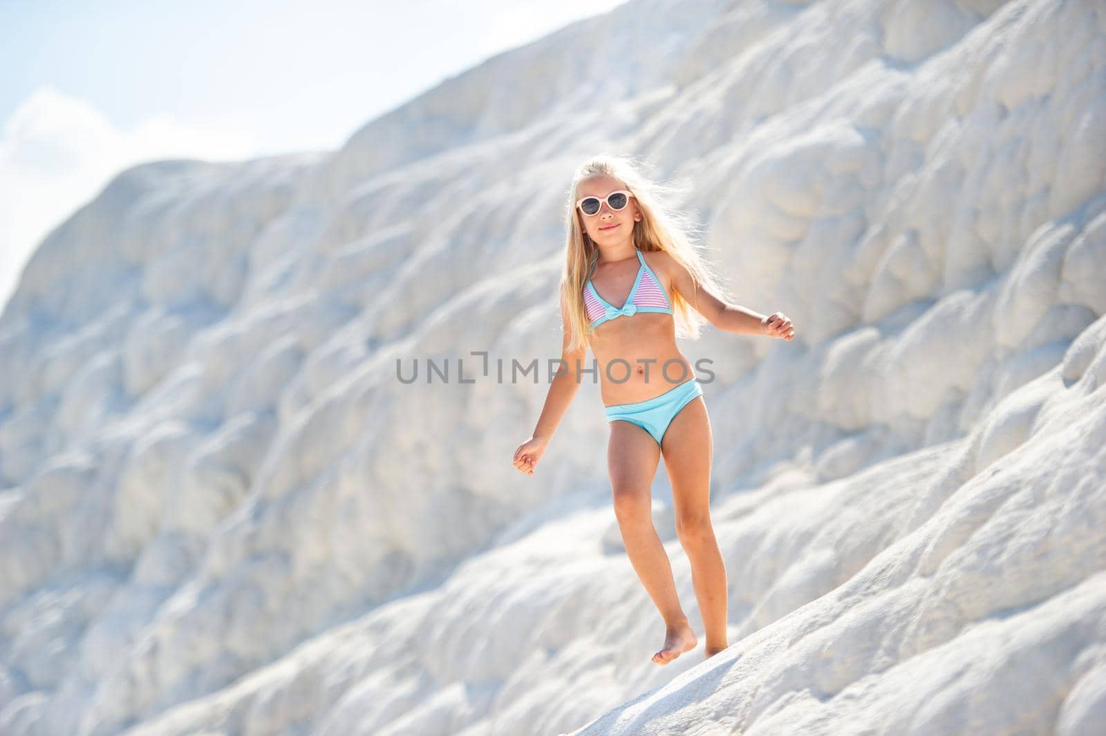 a little girl in a swimsuit and sunglasses on the White Salt Mountain in Pamukkale .Turkey by Lobachad