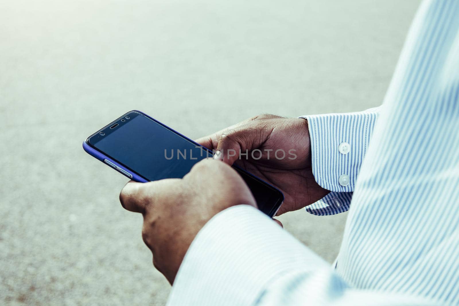 Very close-up view of dark skinned hands using mobile phone outdoors.