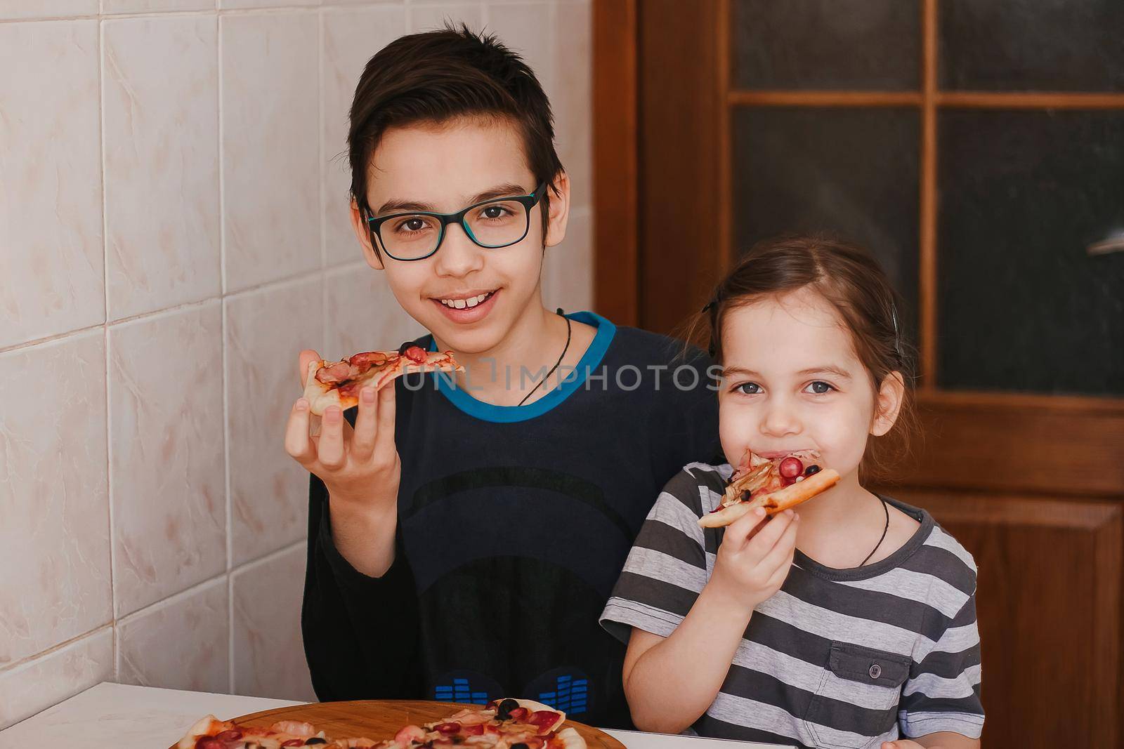 Happy children boy and girl eating pizza at home