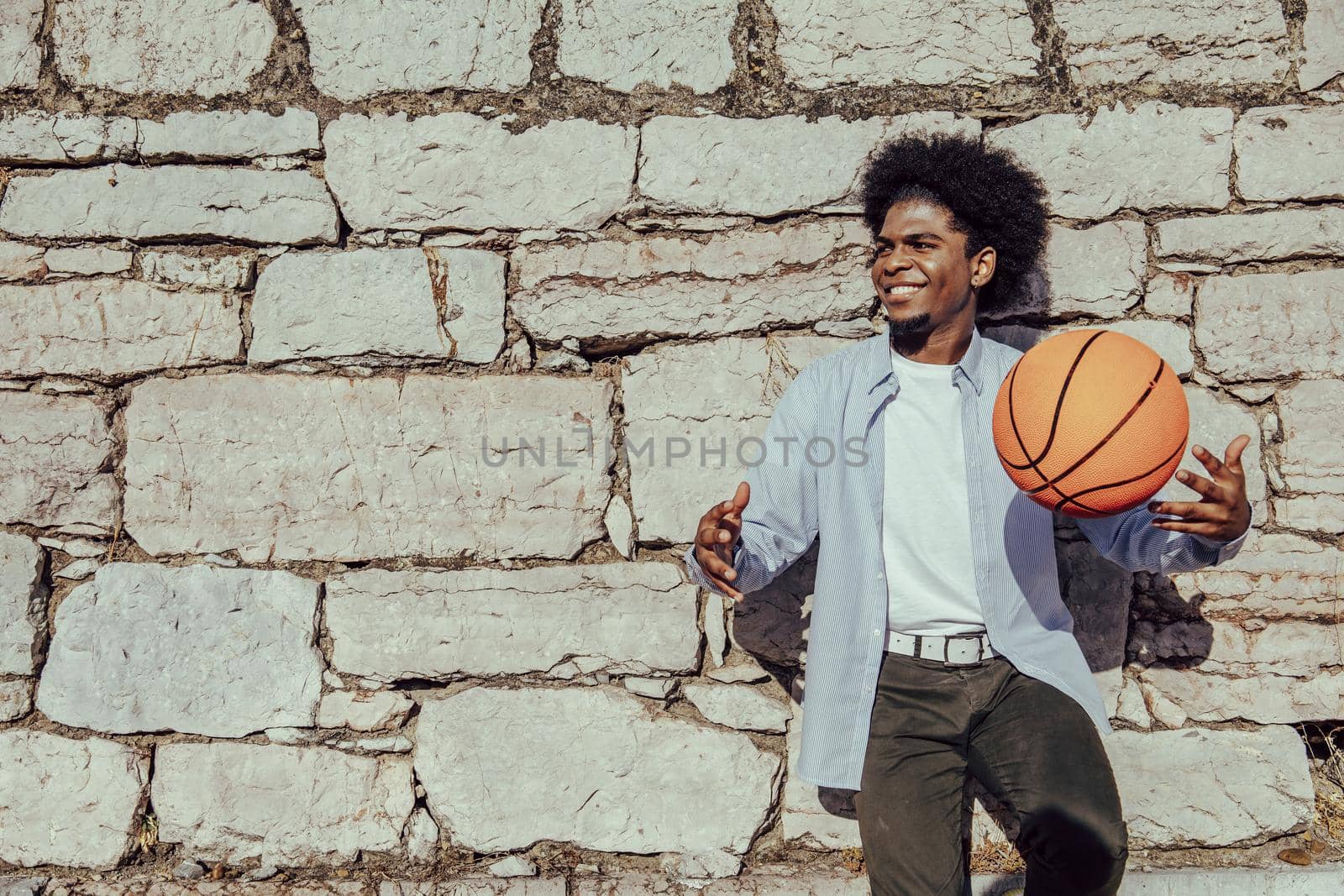 Happy afro hair dark skinned man with basket ball leaning on wall. Copy space by ALVANPH