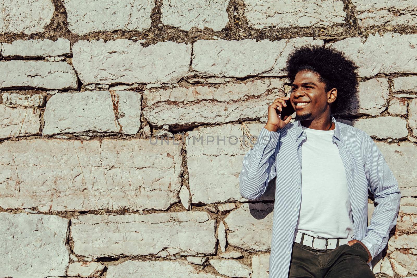 young african man with afro talking on mobile phone leaning on wall