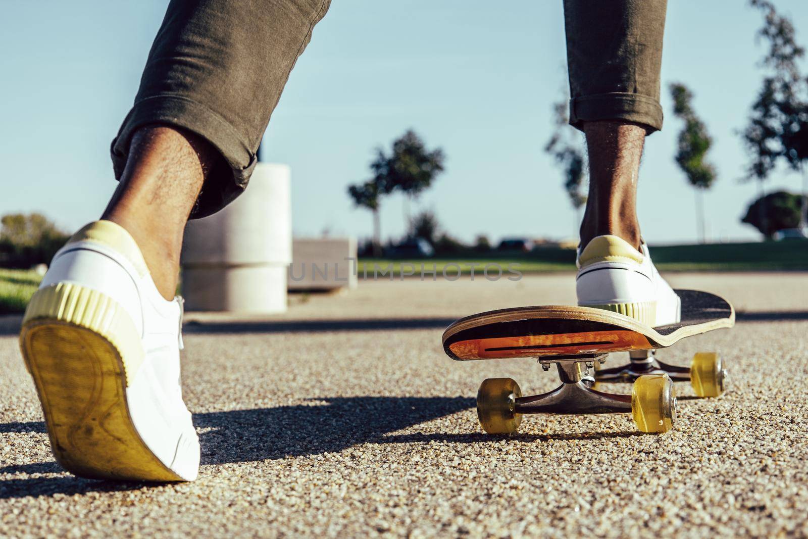Closeup of dark skin legs riding skateboard in park by ALVANPH