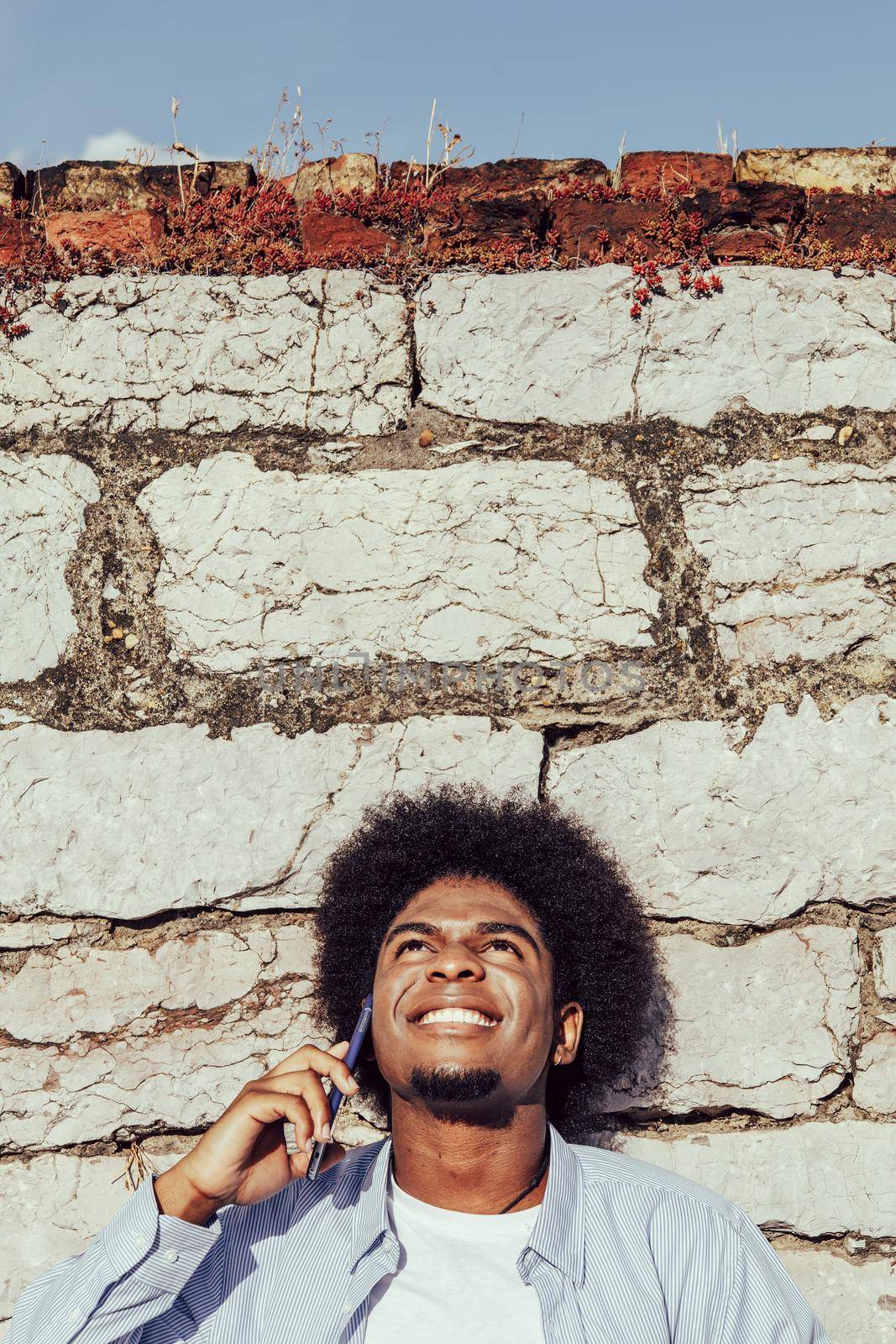 young afroamerican man with afro talking on mobile phone leaning on wall