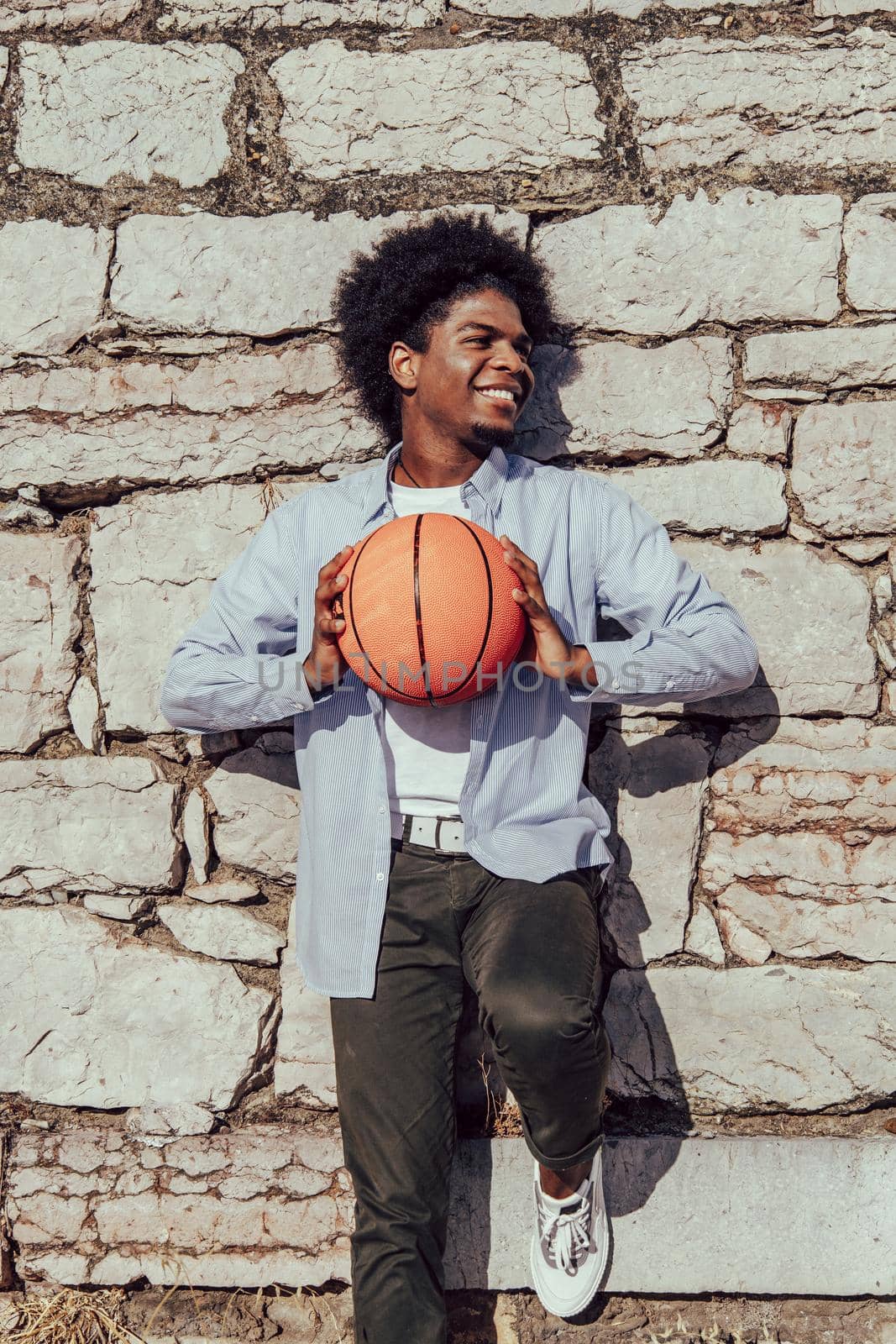 young american man with afro hair leaning on wall with basket ball by ALVANPH