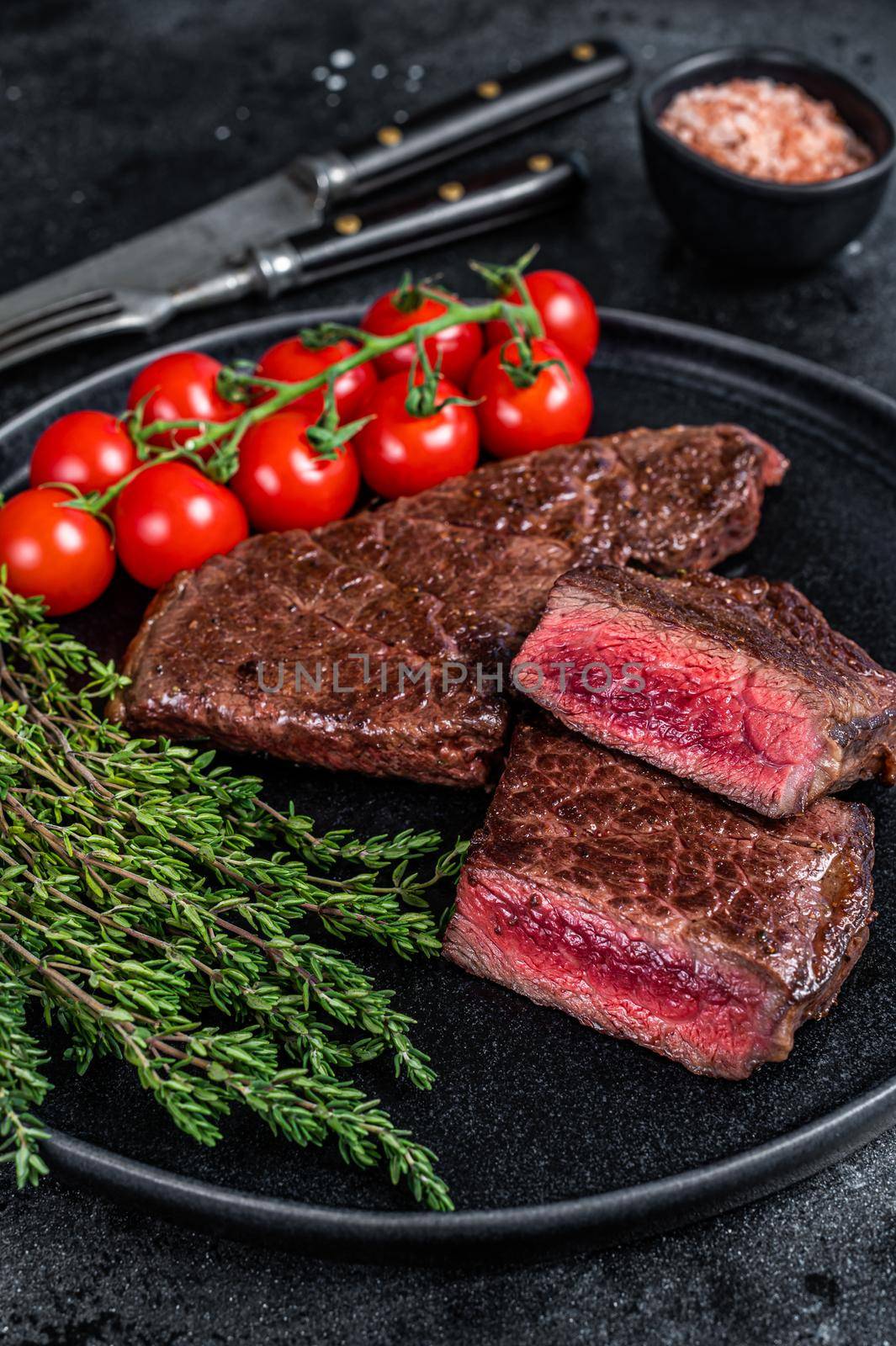 Roasted cut denver beef meat steak on a plate with thyme. Black background. Top view.