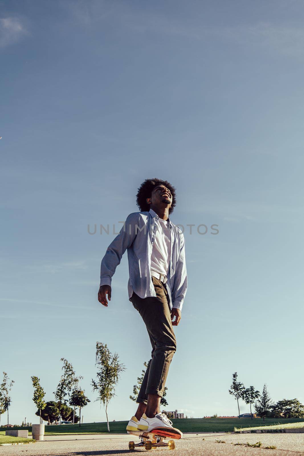 Young black ethnicity man with afro hair skateboarding and looking up to the sky by ALVANPH