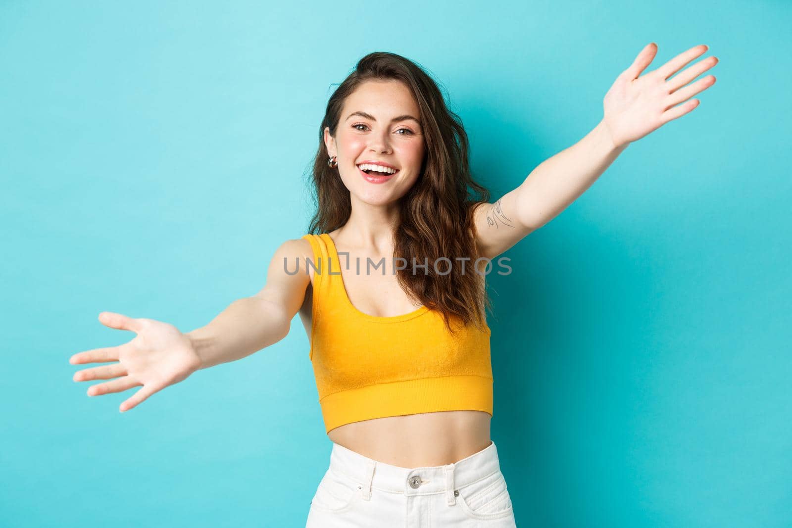 Summer and lifestyle concept. Attractive friendly woman stretch out hands and smiling happy, inviting you for hug, welcome or greet friend, standing over blue background.