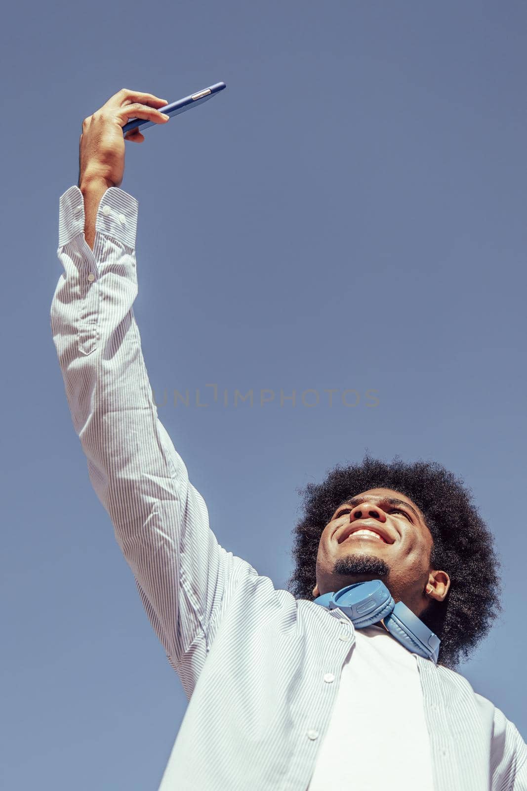 Vertical portrait of young african american man with afro hair taking selfie. View from below by ALVANPH