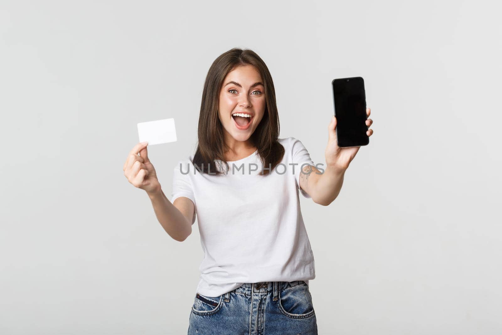 Attractive smiling girl looking satisfied and showing credit card, mobile phone screen.
