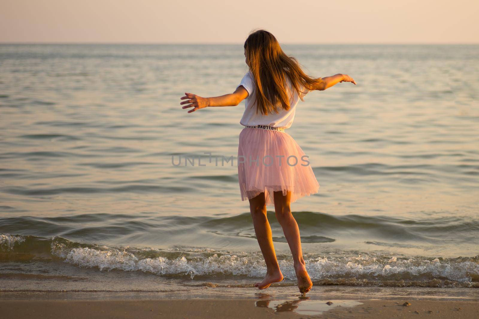 Happy little girl is spinning and dancing on the beach on a Sunny day