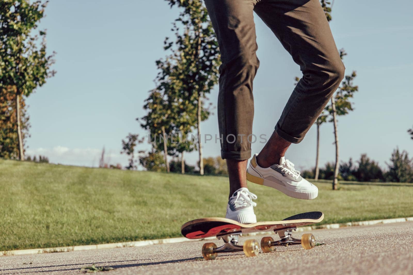 unrecognizable legs of african young man skateboarding in park