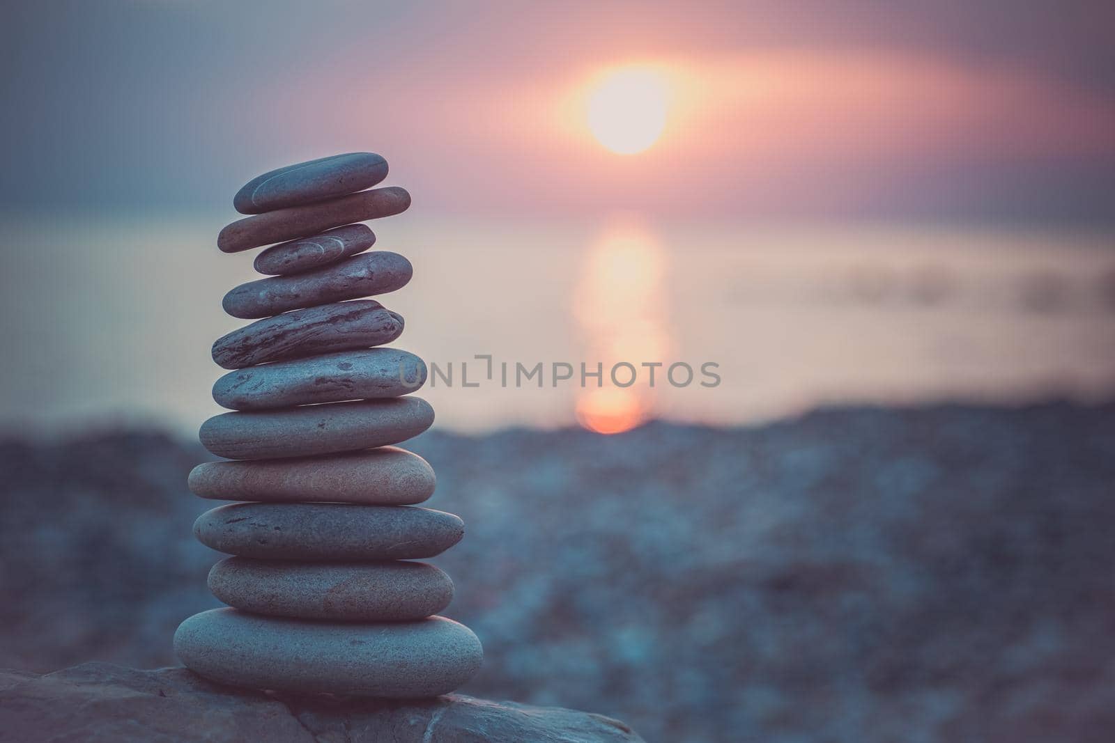 Stones pyramid on sand symbolizing zen, harmony, balance. Ocean at sunset in the background.