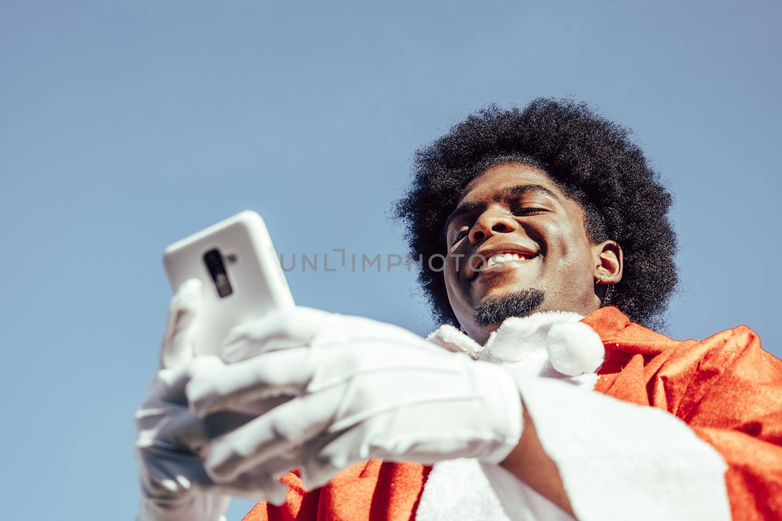 African american santa claus using smartphone from below. Sky background