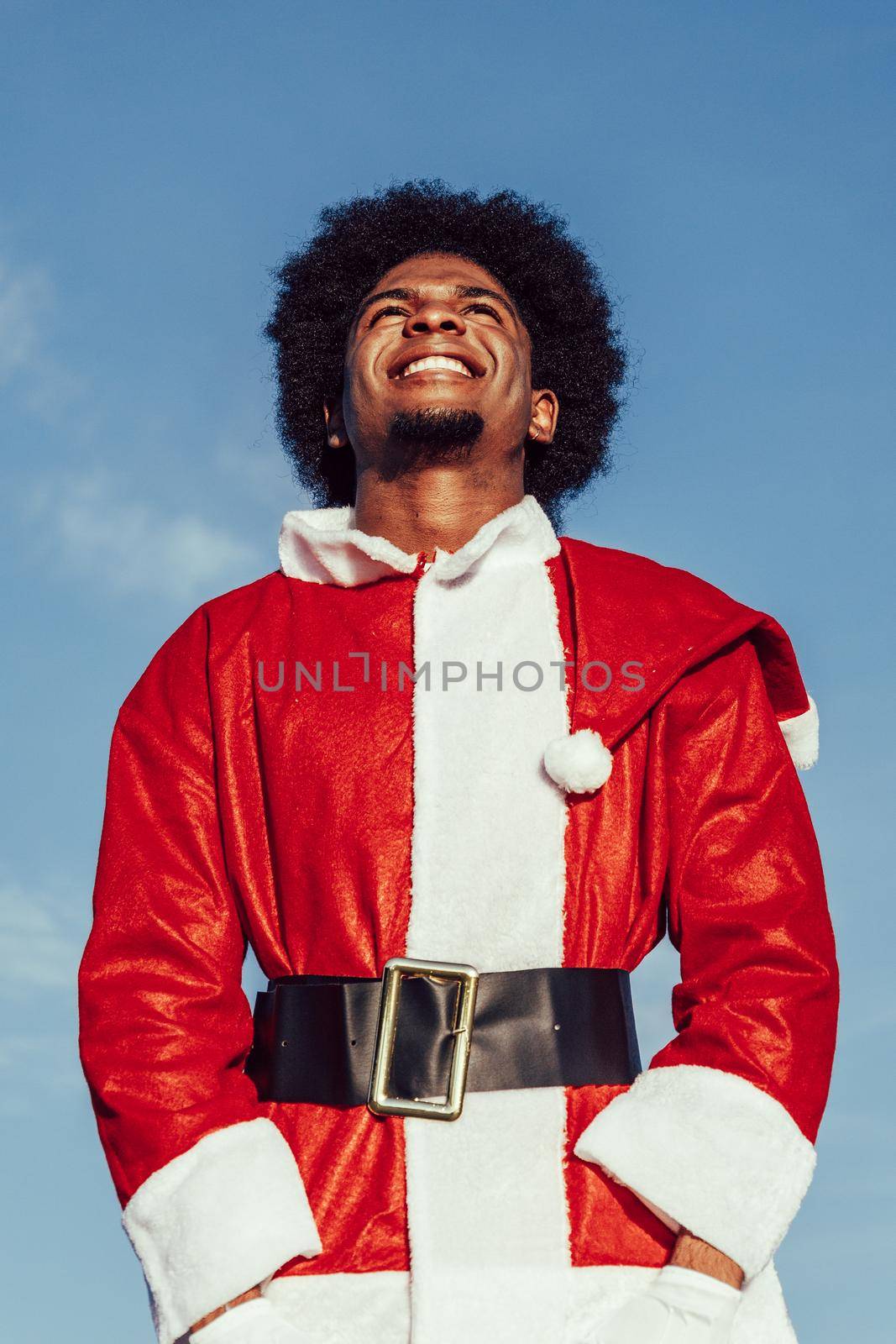 african american santa claus with afro hair looking up and smiling over sky background