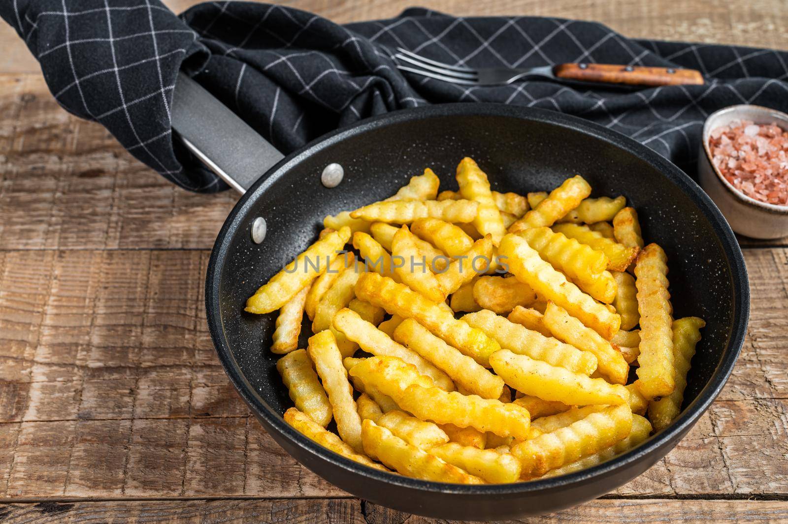 Fried Crinkle oven French fries potatoes sticks in a pan. Wooden background. Top view.