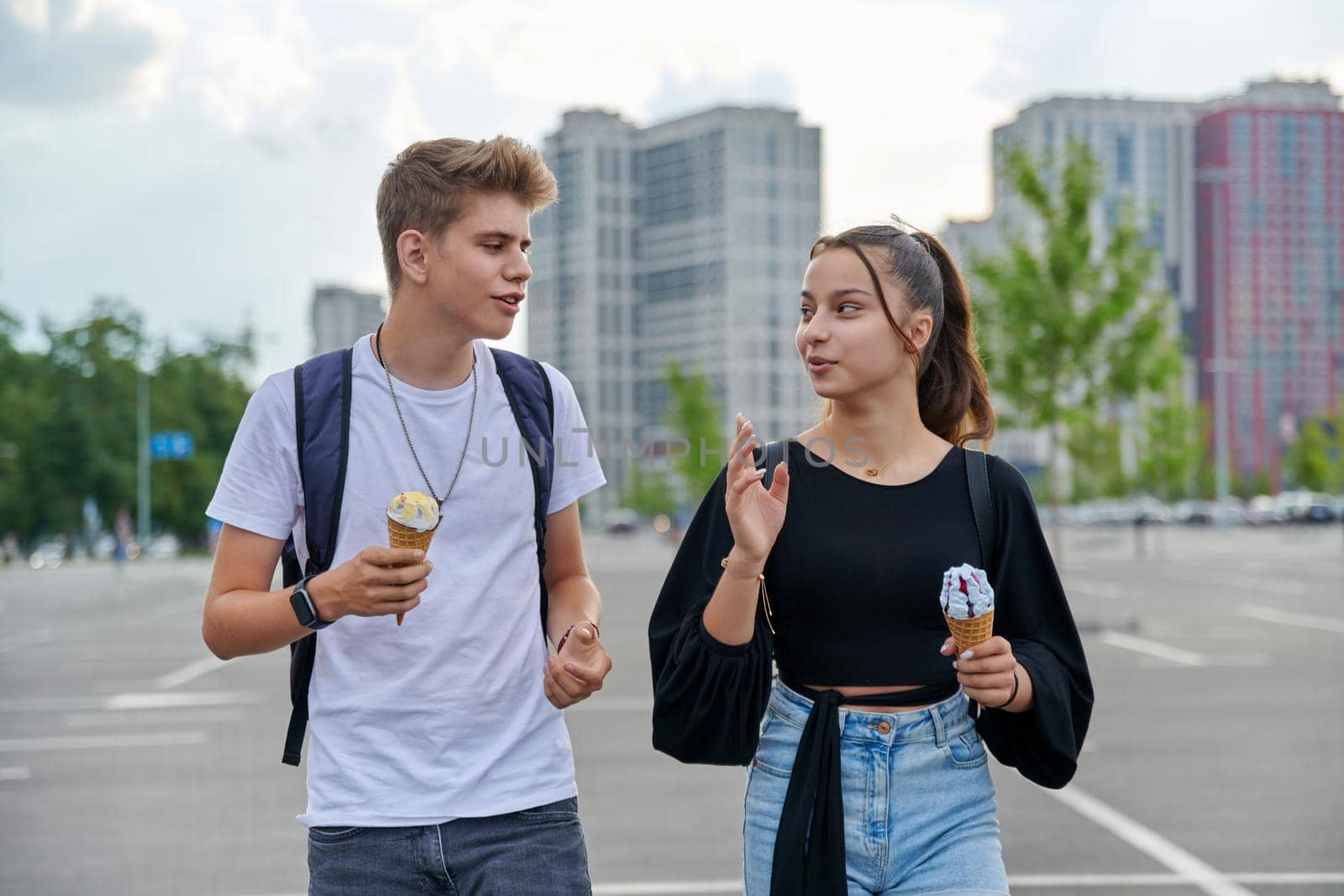 Happy talking couple of teenagers walking together in city, guy and teenage girl with ice cream, friendship, relationship, summer, leisure, lifestyle, adolescence concept