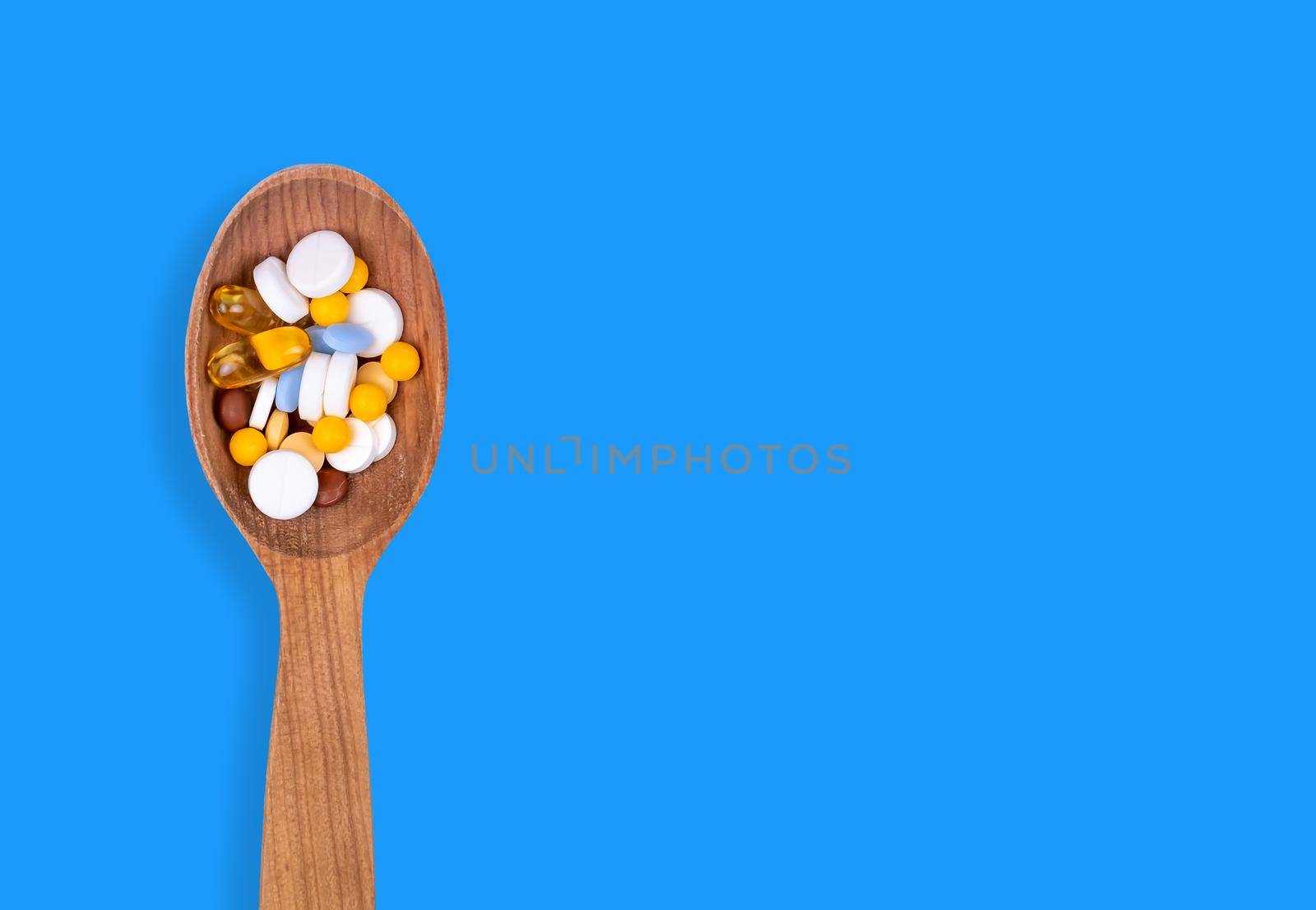 Medicine, pills and drug in wood spoon on blue background with copy space