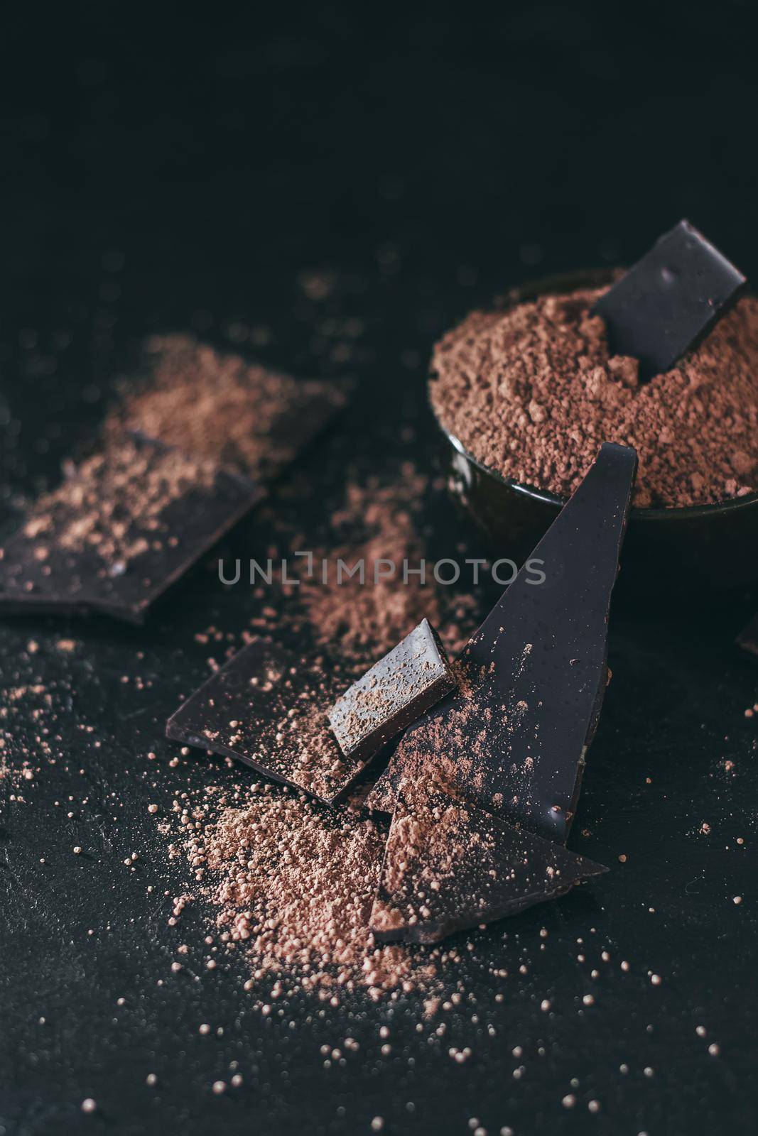 Chocolate bar pieces with cocoa powder on dark background, cope space.