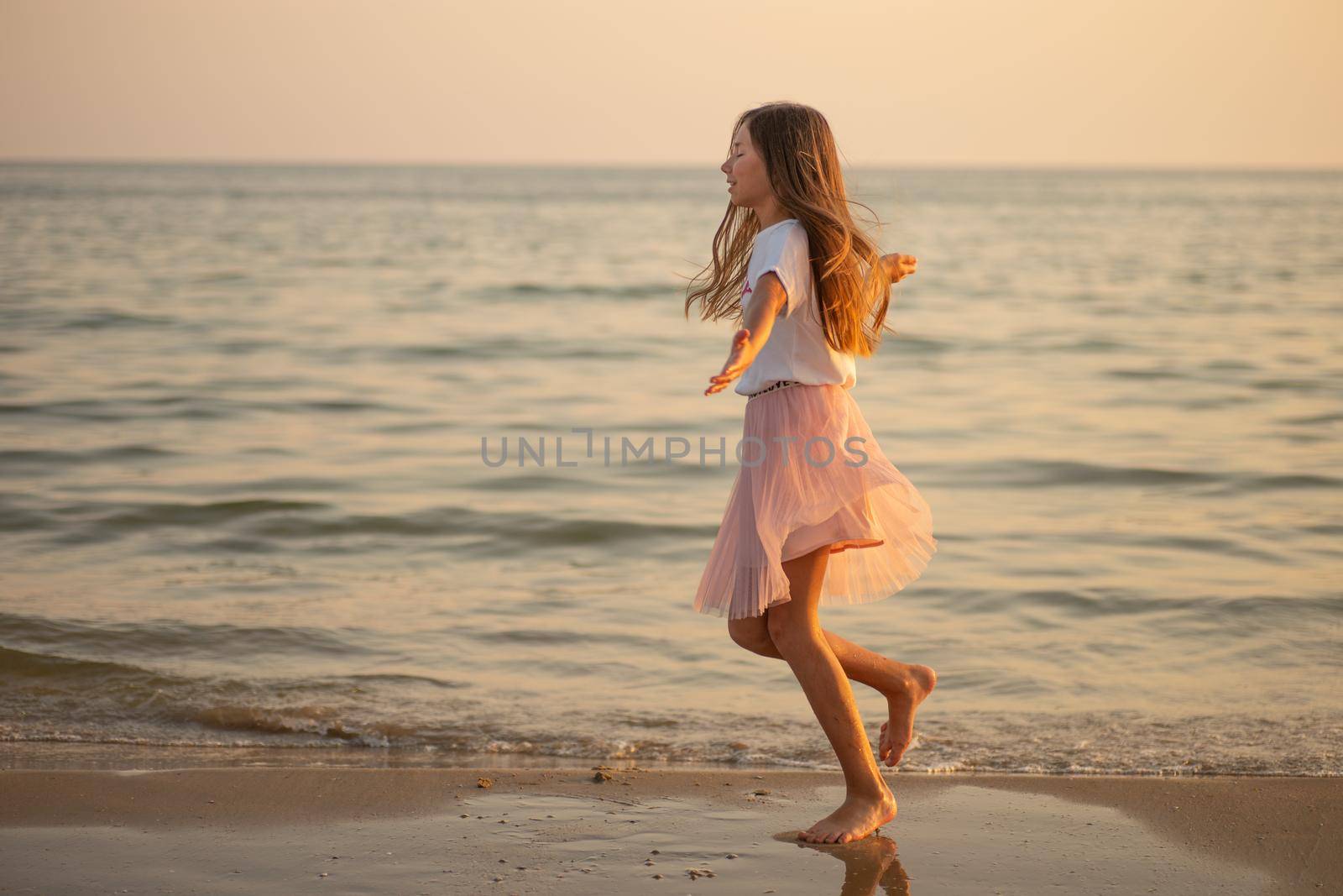 Happy little girl is spinning and dancing on the beach on a Sunny day