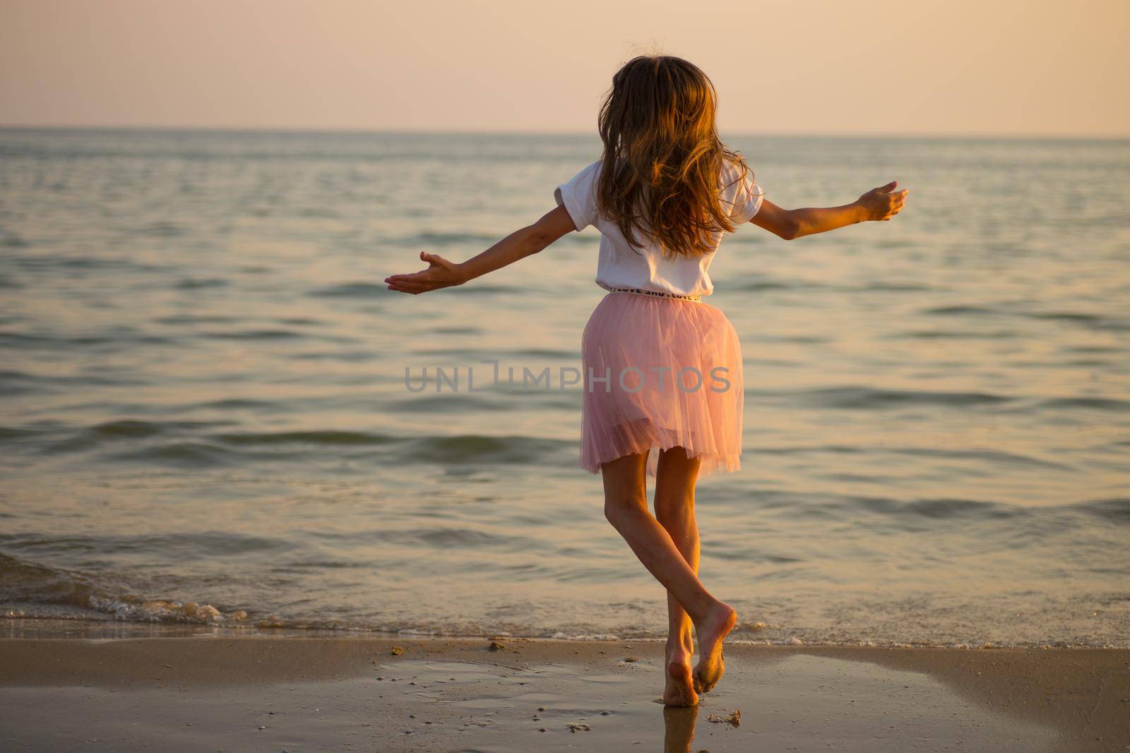 Happy little girl is spinning and dancing on the beach on a Sunny day. by alf061