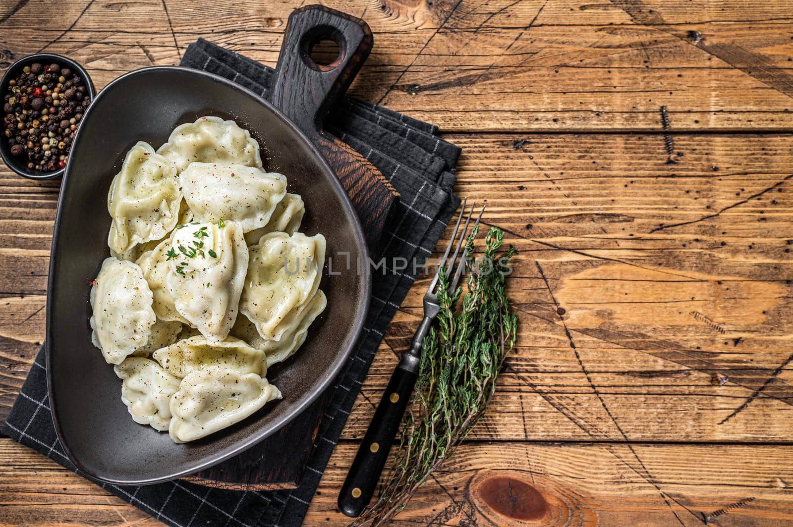 Dumplings pierogi with potato in a plate with herbs and butter. Wooden background. Top View. Copy space.