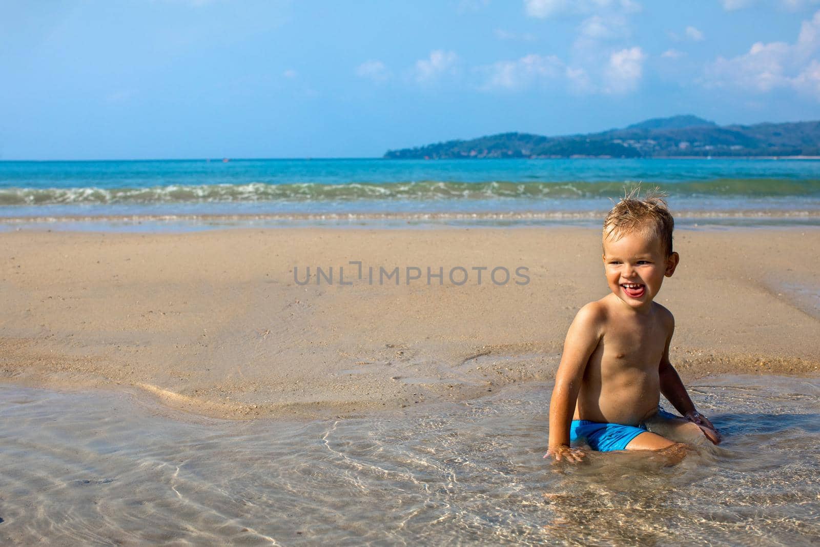 Joyful adorable small boy enjoying water while resting and sitting in water on coastline in summertime
