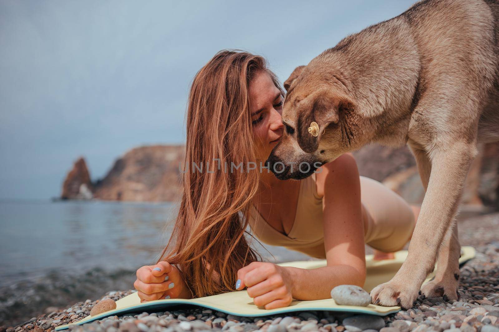 Young woman in beige sportswear with long hair practicing stretching outdoors on yoga mat by the sea on a sunny day. Women's yoga fitness pilates routine. Healthy lifestyle and meditation concept by panophotograph