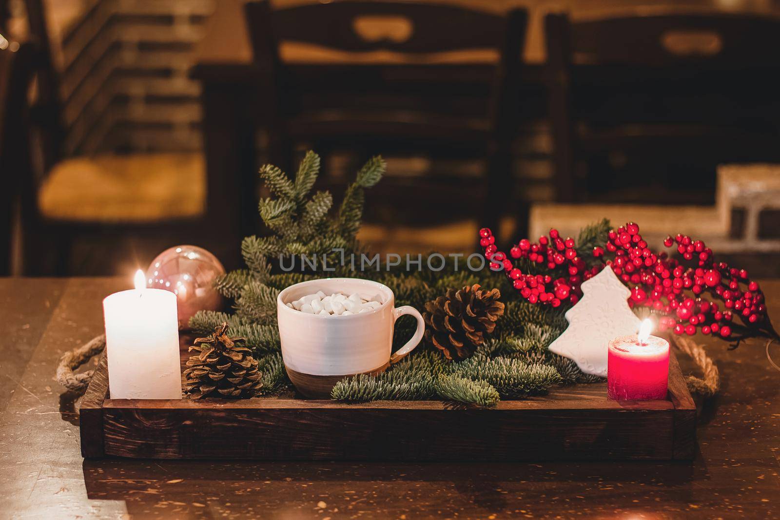 Christmas hot chocolate with mini marshmellows in an old ceramic mug with candles on a wooden background.