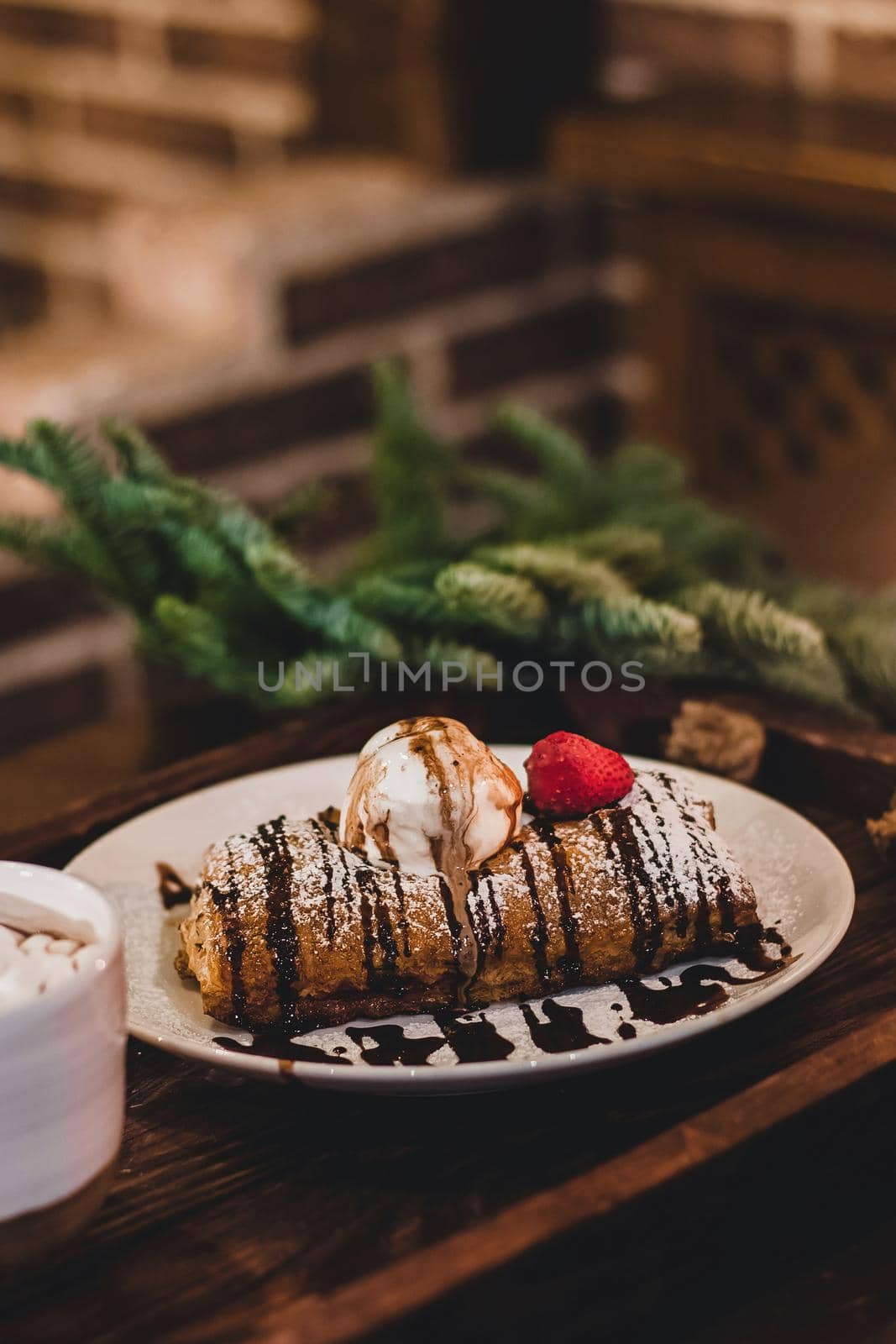 Closeup of a strudel with a strawberry on a Christmas plate near bamboo branch. Christmas breakfast on a wooden table