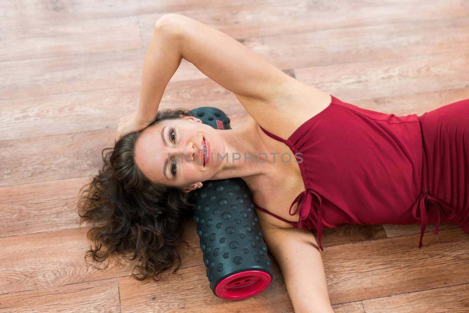 A young woman fitness instructor in red Sportswear Leggings and Top stretching in the gym before her pilates, on a yoga mat near the large window on a sunny day, female fitness yoga routine concept