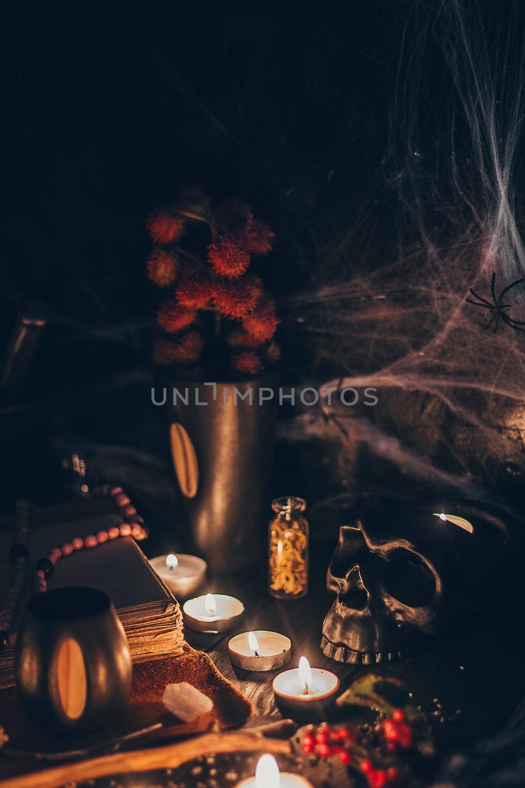 A ritual halloween witchcraft scene with candles, herbs, spider web, vintage bottles on the rustic background with a scary skull face and antique book.