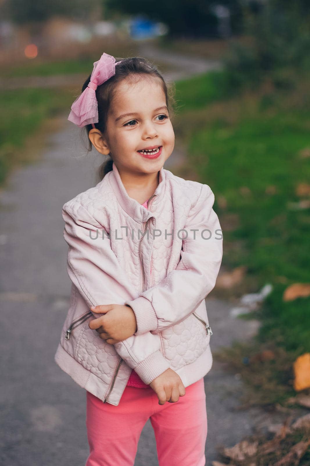 Young smiling girl in a pink jacket and pink leggings in the park