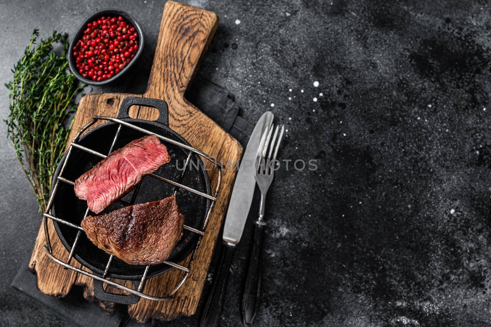 Beef tenderloin steak is grilled on a grill pan. Black background. Top view. Copy space.