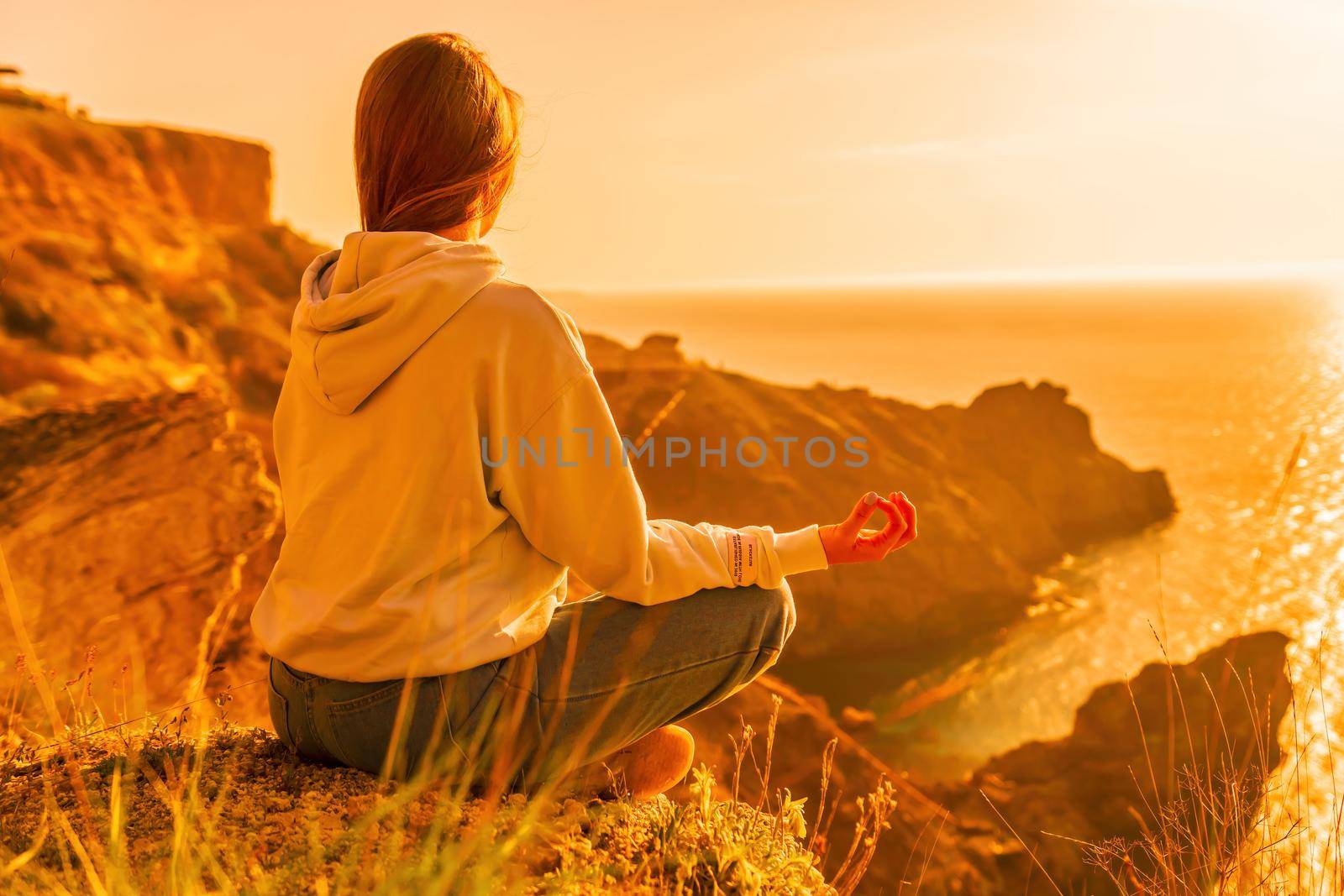 A young tourist Woman enjoying sunset over sea mountain landscape while sitting outdoor. Women's yoga fitness routine. Healthy lifestyle, harmony and meditation by panophotograph