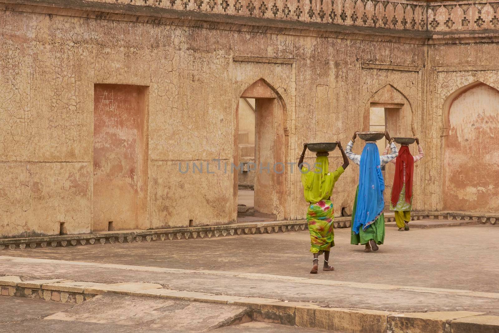 JAIPUR, RAJASTHAN, INDIA - JULY 30, 2008: Female laborers transporting water and plaster in bowls carried on the head during the restoration of a palace inside Amber Fort in Jaipur, Rajasthan, India.