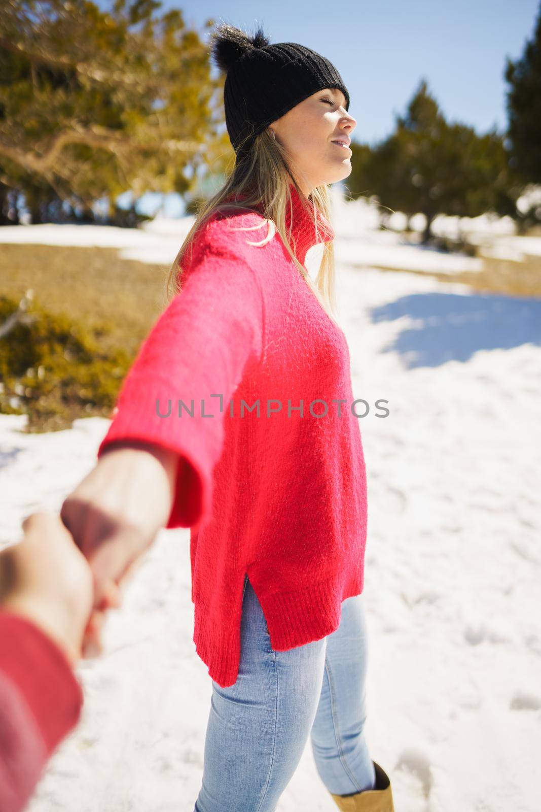 Blonde woman in winter clothes walking holding her partner's hand in the snowy mountains. by javiindy