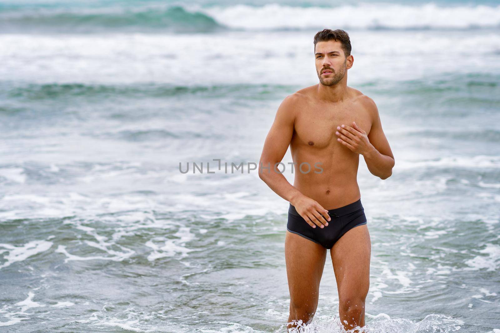 Handsome muscular man bathing on the beach wearing swimwear