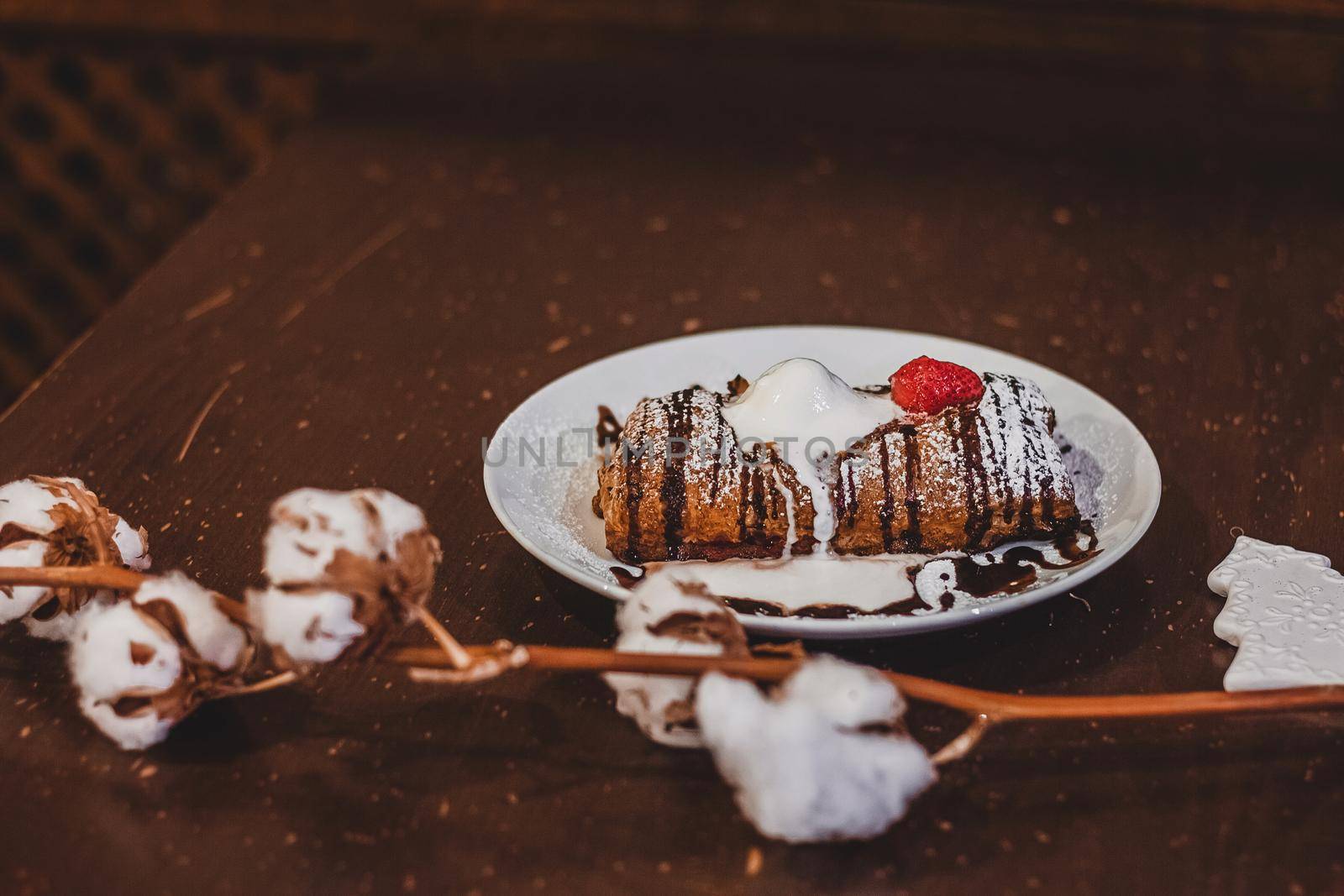 Closeup of a strudel with a strawberry on a Christmas plate near bamboo branch. Christmas breakfast on a wooden table