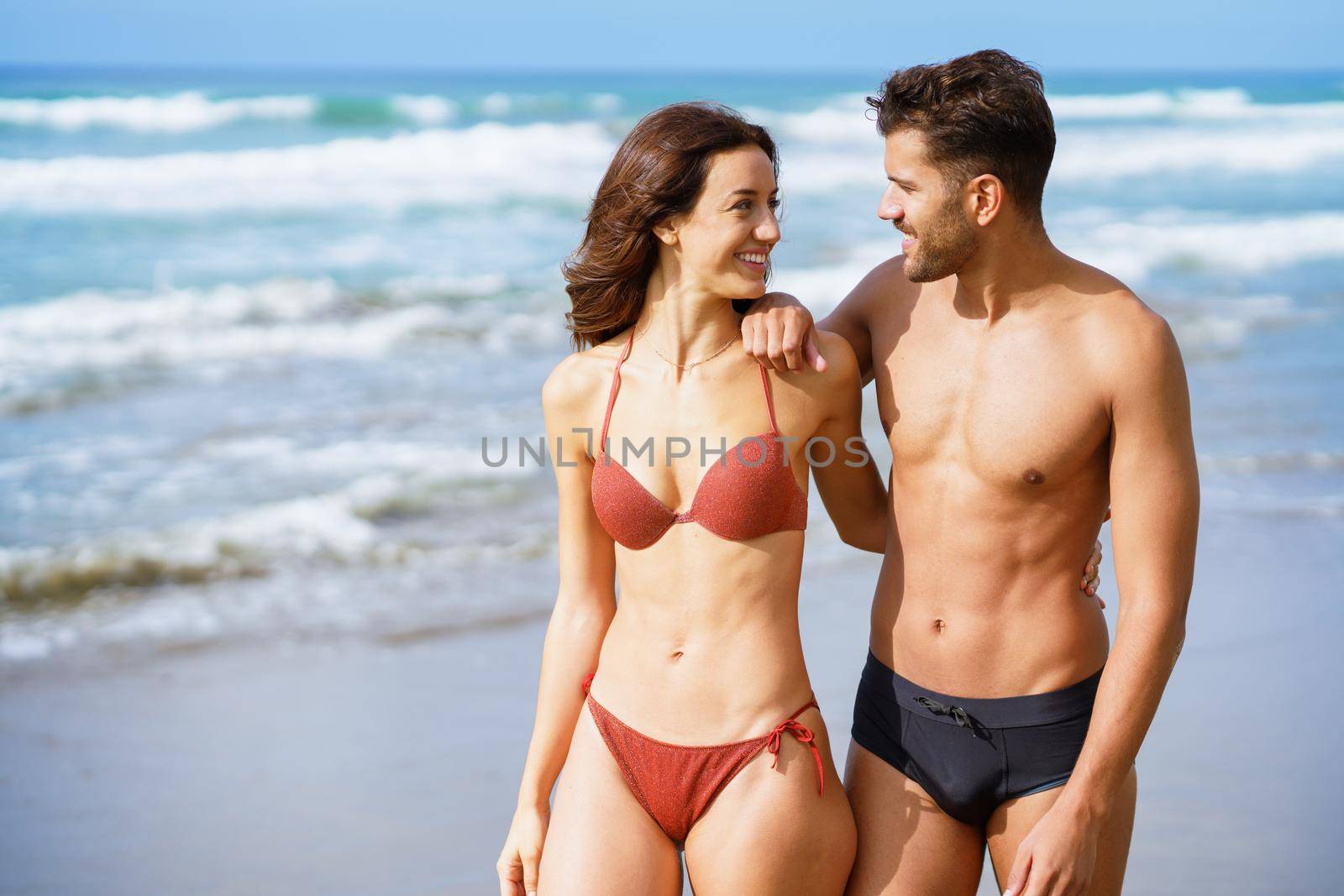 Young couple of beautiful athletic bodies walking together on the beach by javiindy