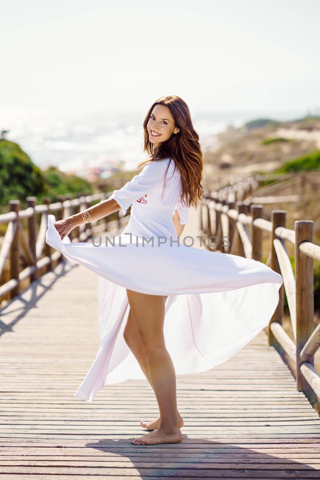 Young woman wearing a beautiful white dress in Spanish fashion on a boardwalk on the beach. by javiindy