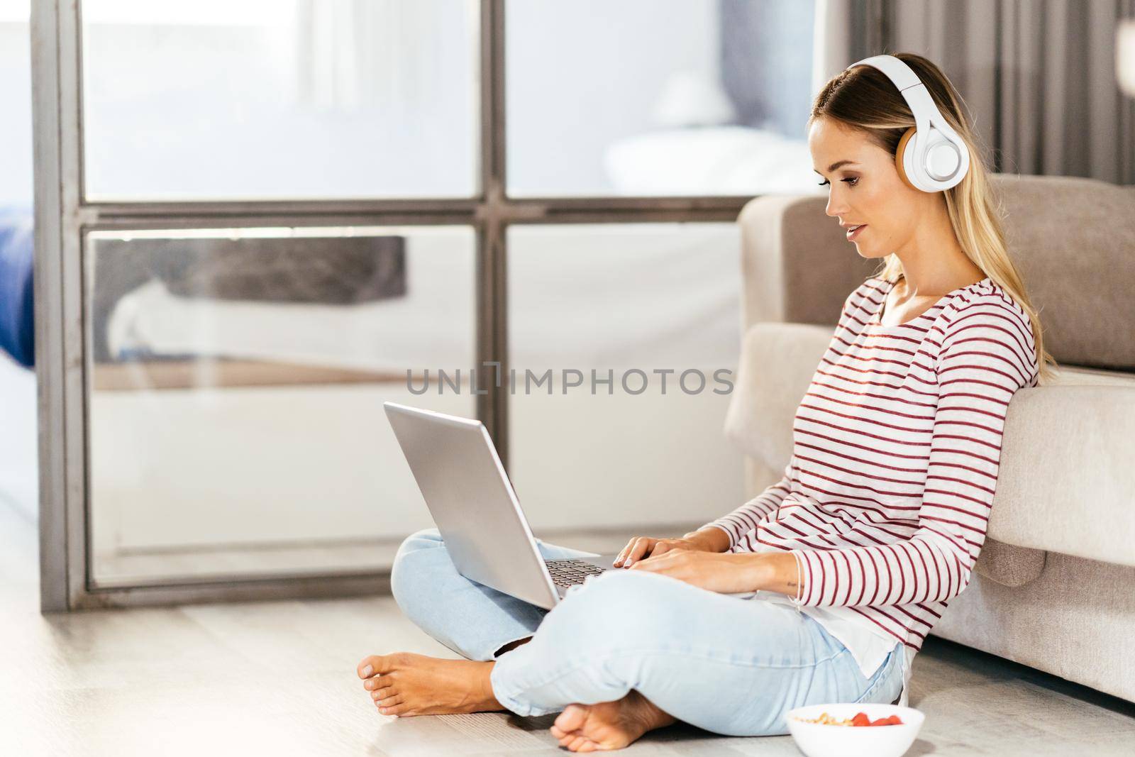 Young woman with headphones and laptop on the sofa at home.