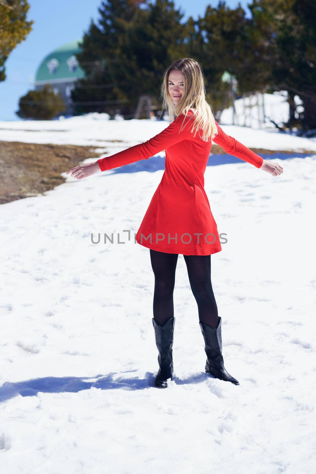 Young blonde woman wearing a red dress and black stockings opening her arms in happiness in the snowy mountains, in Sierra Nevada, Granada, Spain.