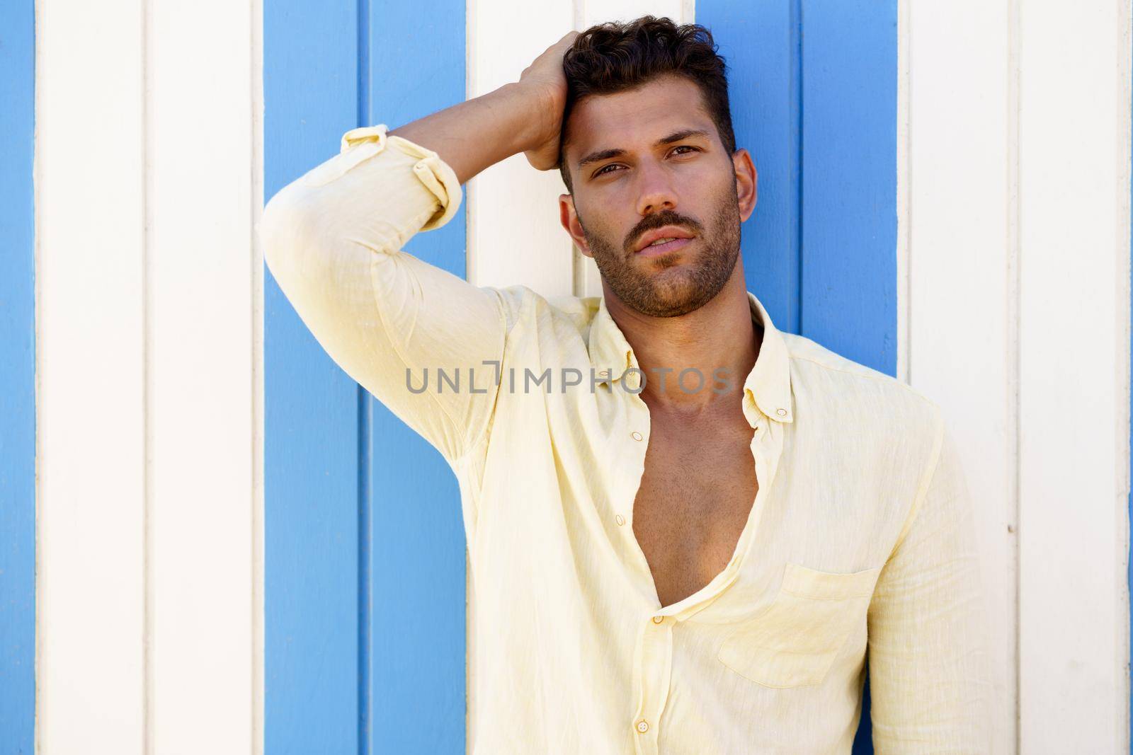 Young man, fashion model, posing in front of a beach booth. by javiindy