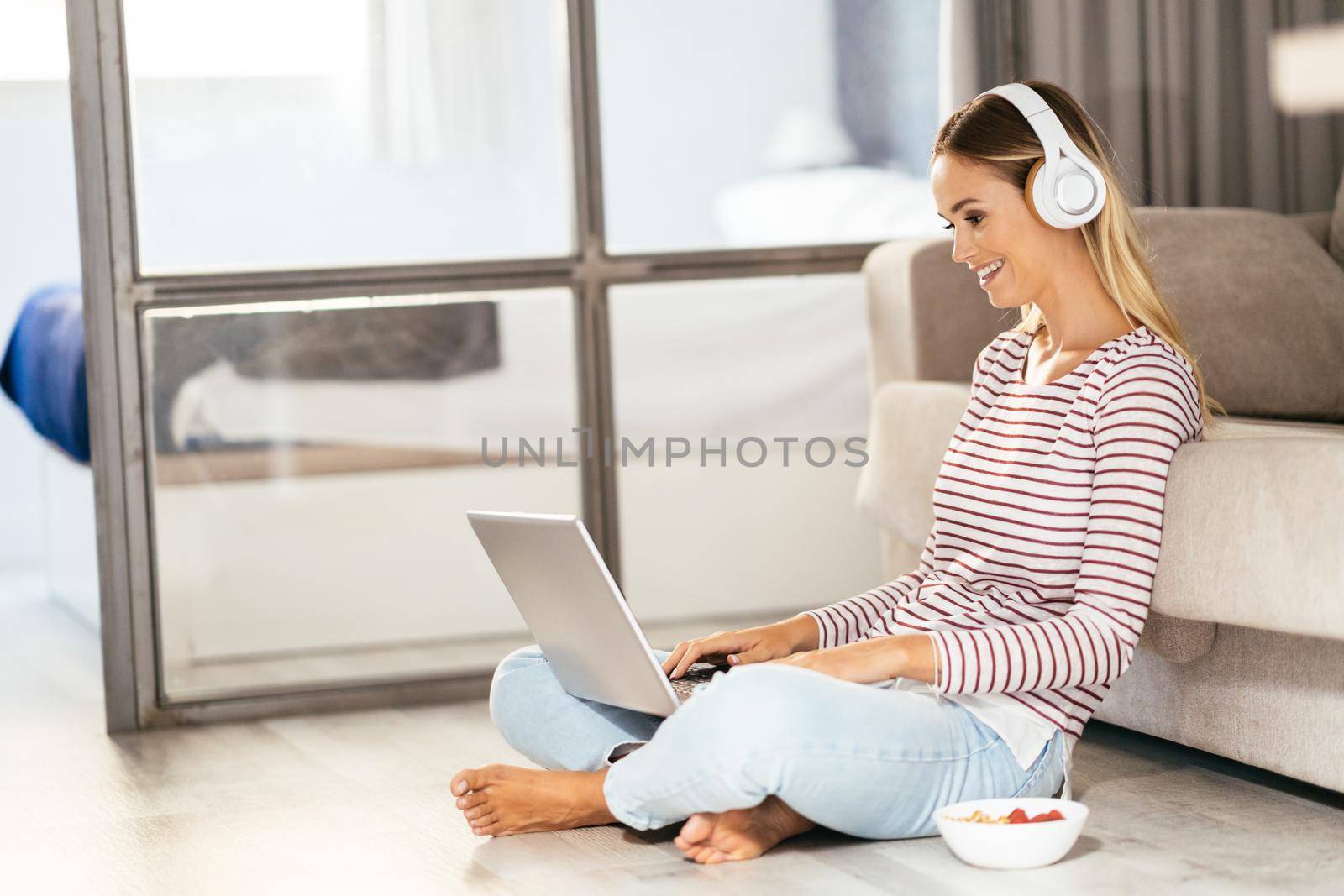 Smiling young woman with headphones and laptop on the sofa by javiindy