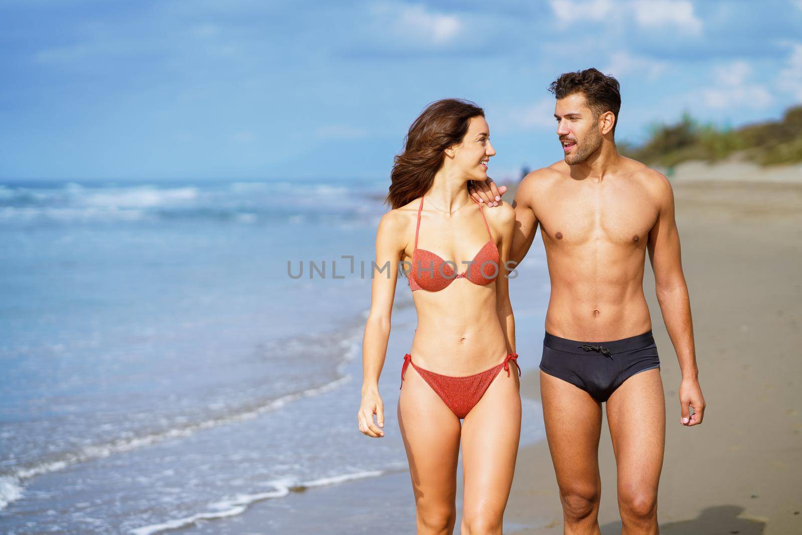 Young couple of beautiful athletic bodies walking together on the beach by javiindy