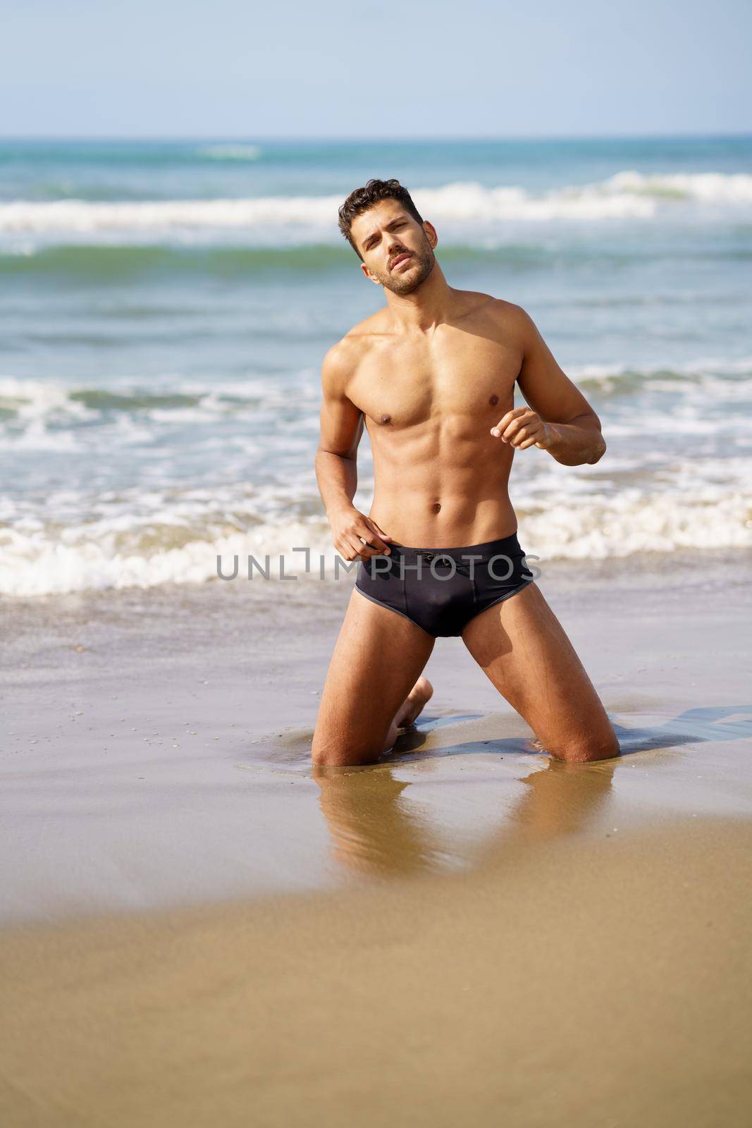 Handsome man on his knees on the sand of the beach by javiindy