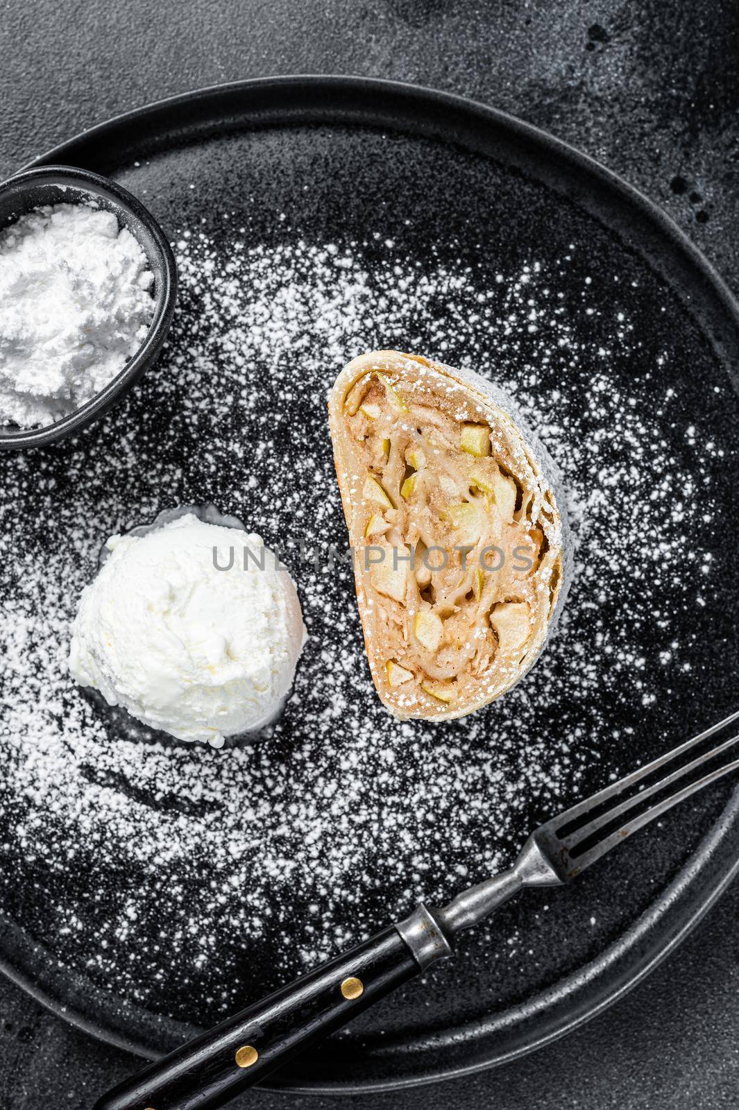 Apple strudel with cinnamon, powdered sugar and vanilla ice cream on a plate. Black background. Top view.